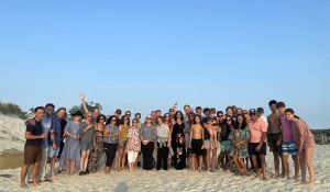 A group of about 35 people standing together on the beach posing for the photo.